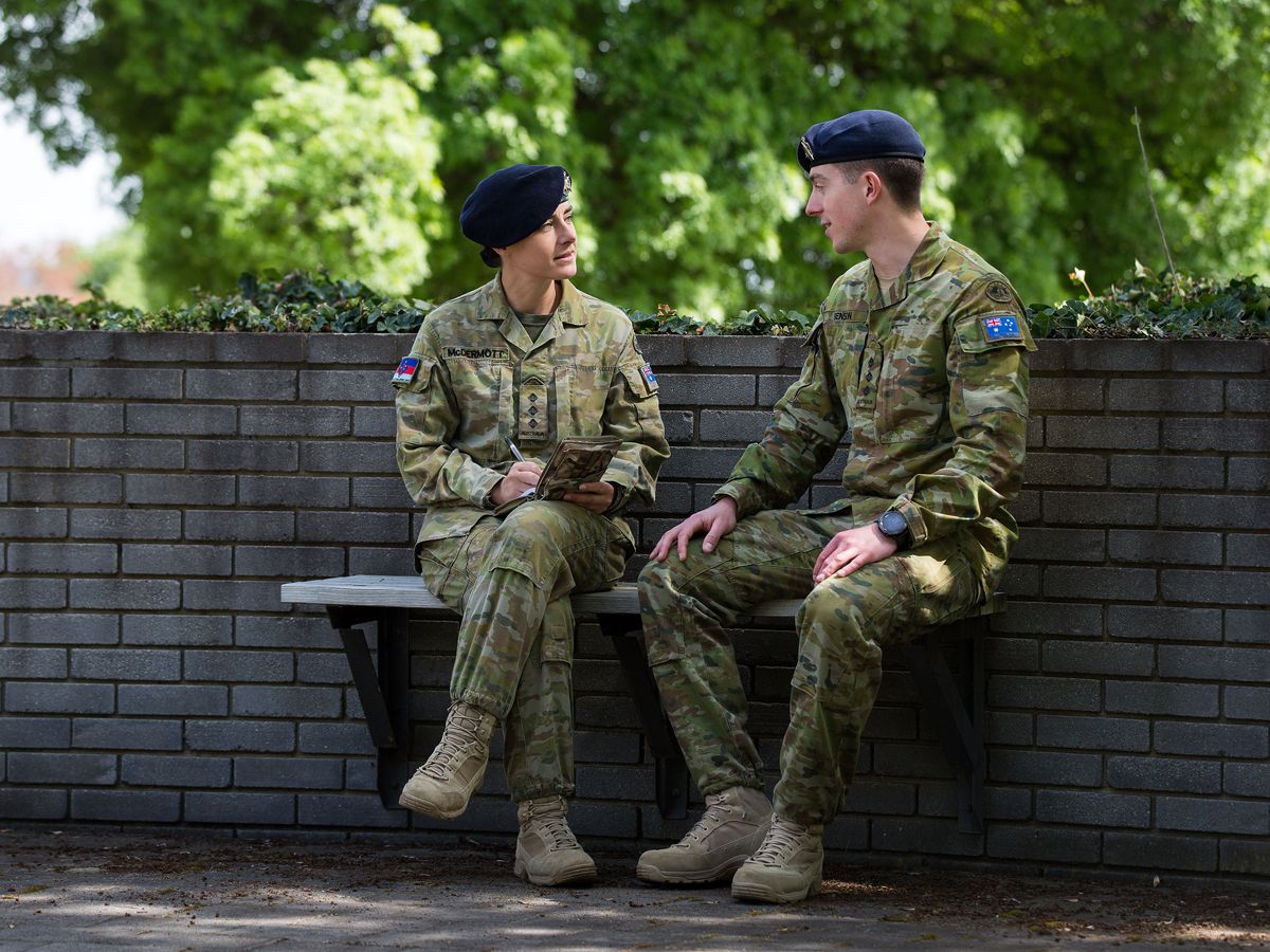 Two members of the Army discuss matters outside on a bench.
