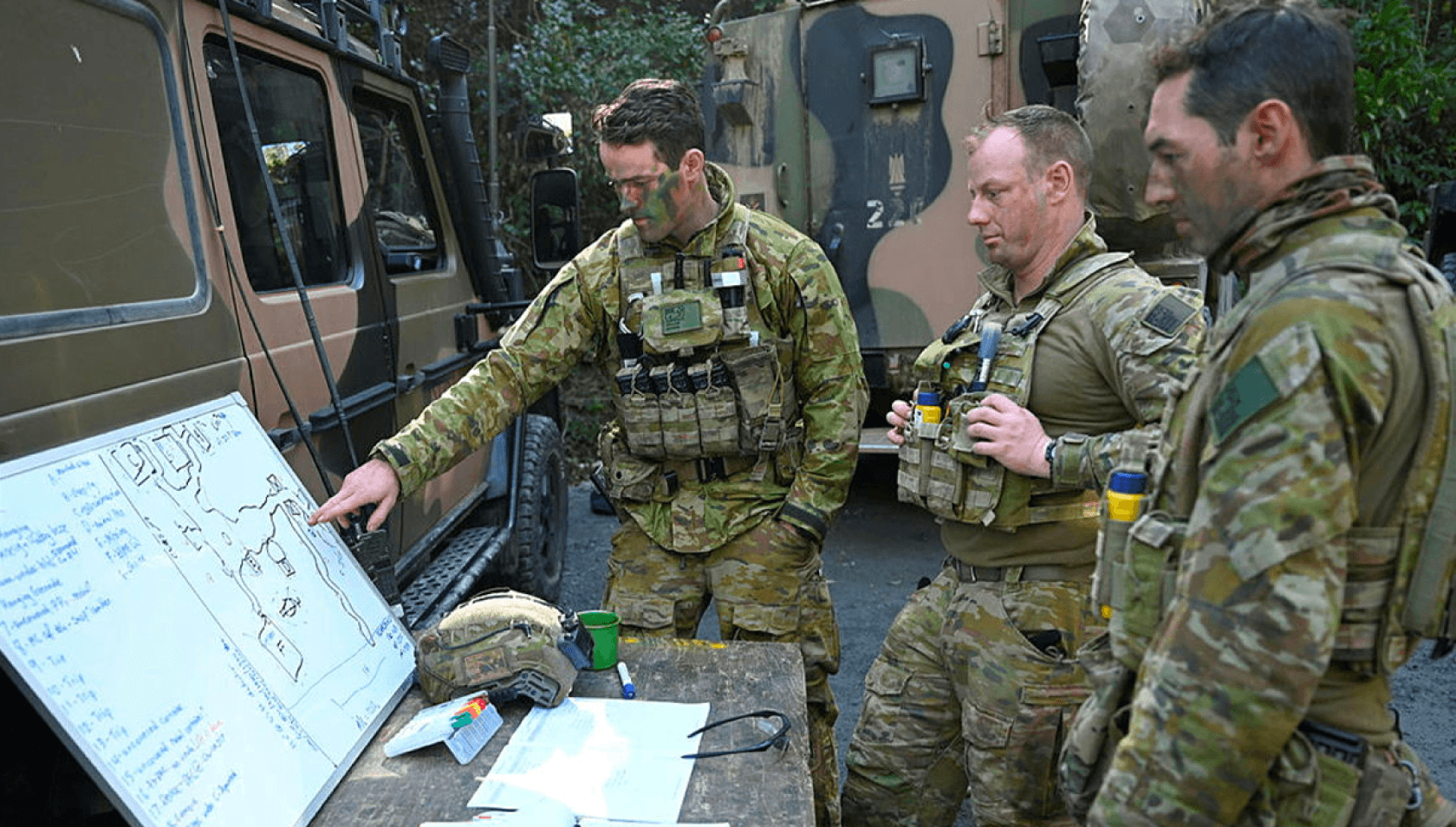 Army personnel discuss the stragey on a whiteboard.