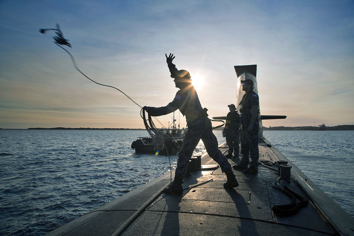Members of the Navy standing on top of a submarine throwing a rope.
