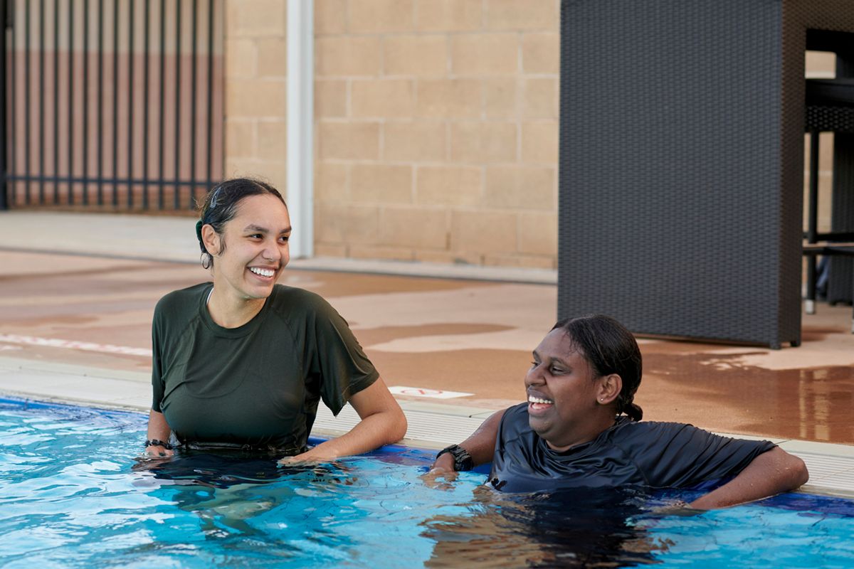 Two women stand in a pool smiling.