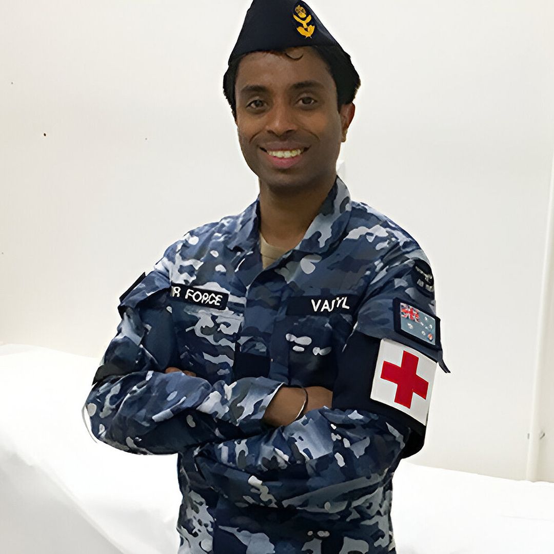 Aviation Medical Officer Ashish stands with his arms crossed in his Air Force uniform, a red medical cross on his arm.