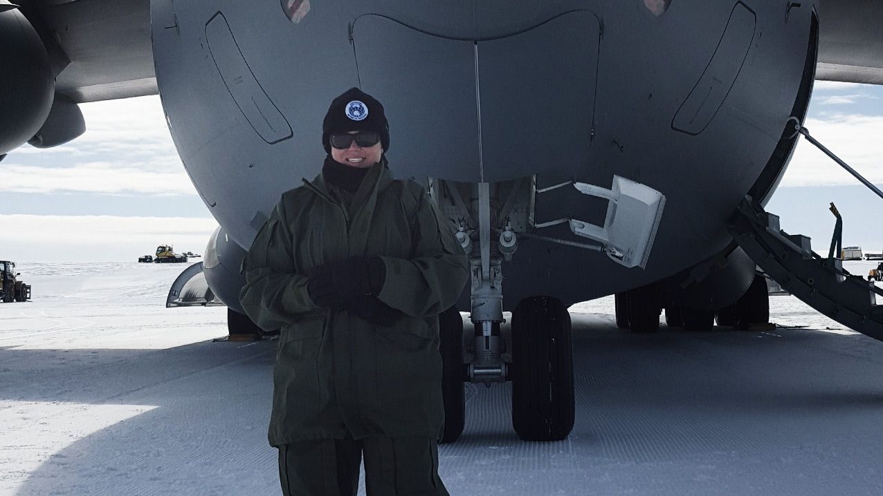 Mel stands on a snow-covered runway in front of an aircraft.