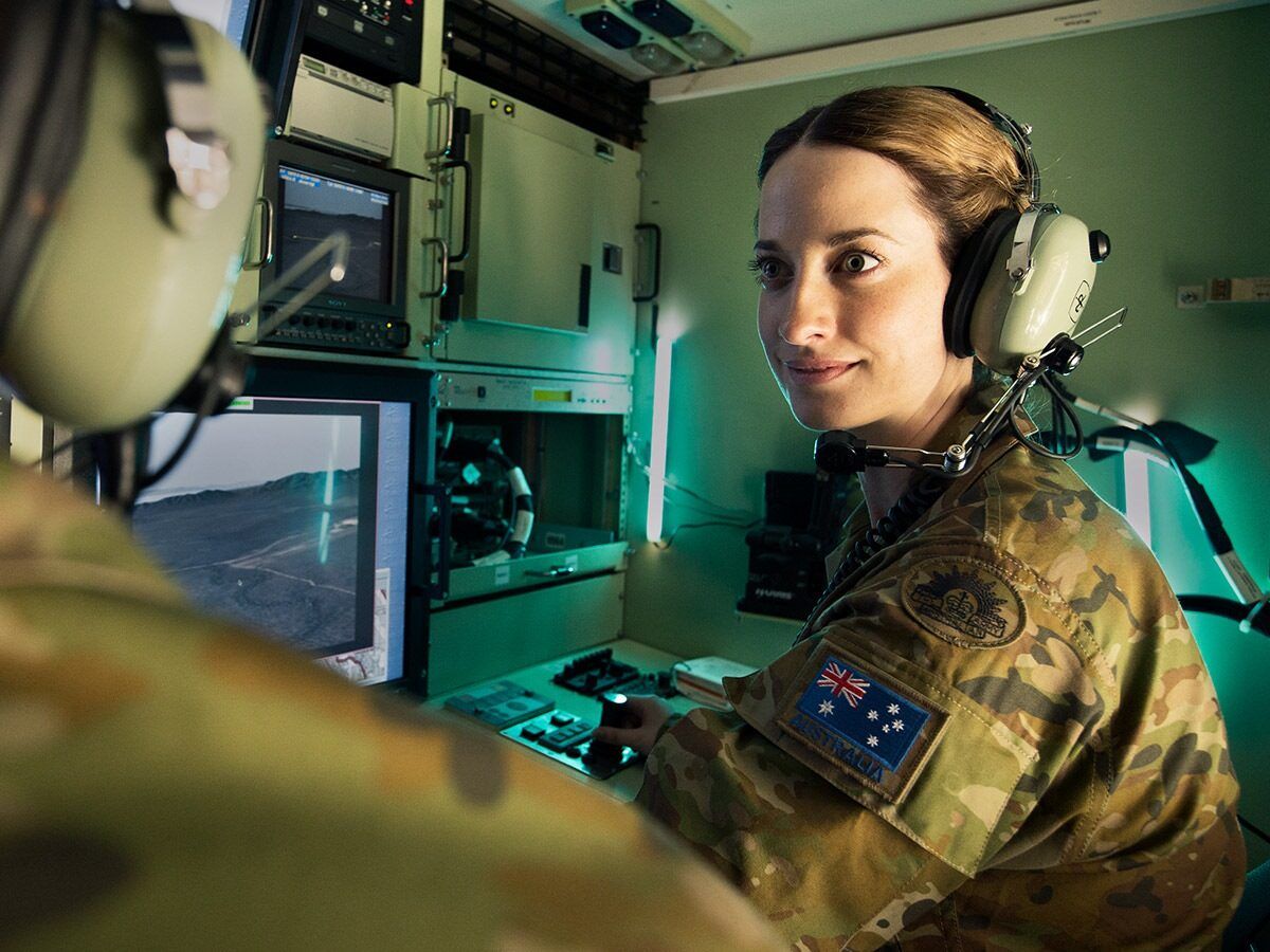In front of a digital screen, Army Officer Ellie looks toward her colleague.