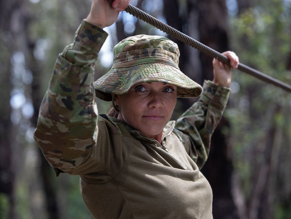Jen wears combat gear, holding onto a thick wire.
