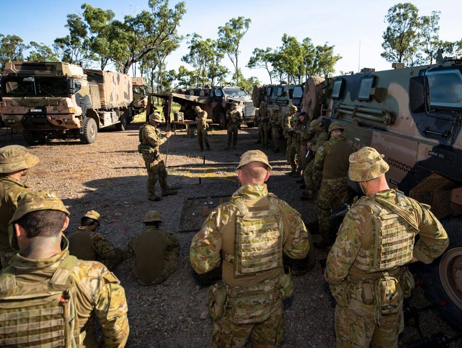 A group of Army members are in the outback preparing for an excersise. 