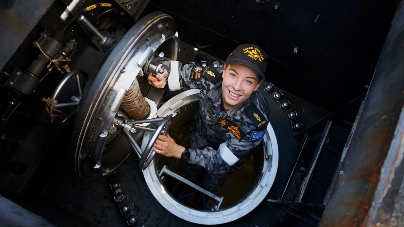 A Navy member climbing out of a submarine smiling. 