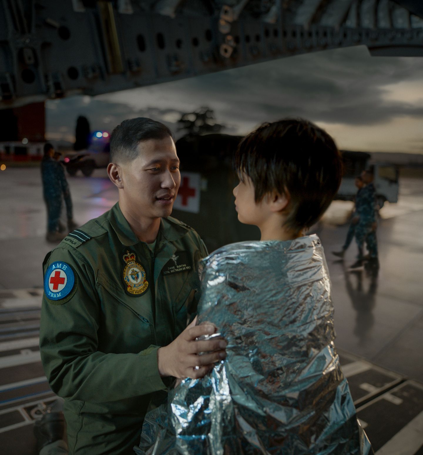 A member of the Air Force wrapping a blanket around a child.