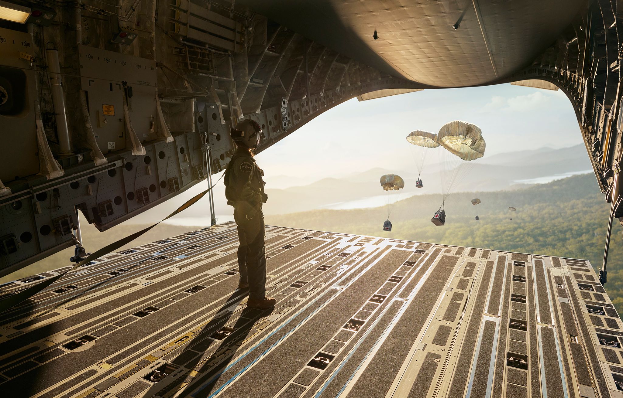 A member of the Air Force watches parachutes deploy out the back of a plane.