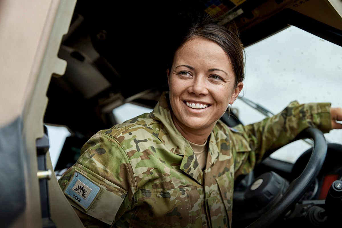 A member of the Army in uniform in the driver's seat of a vehicle.
