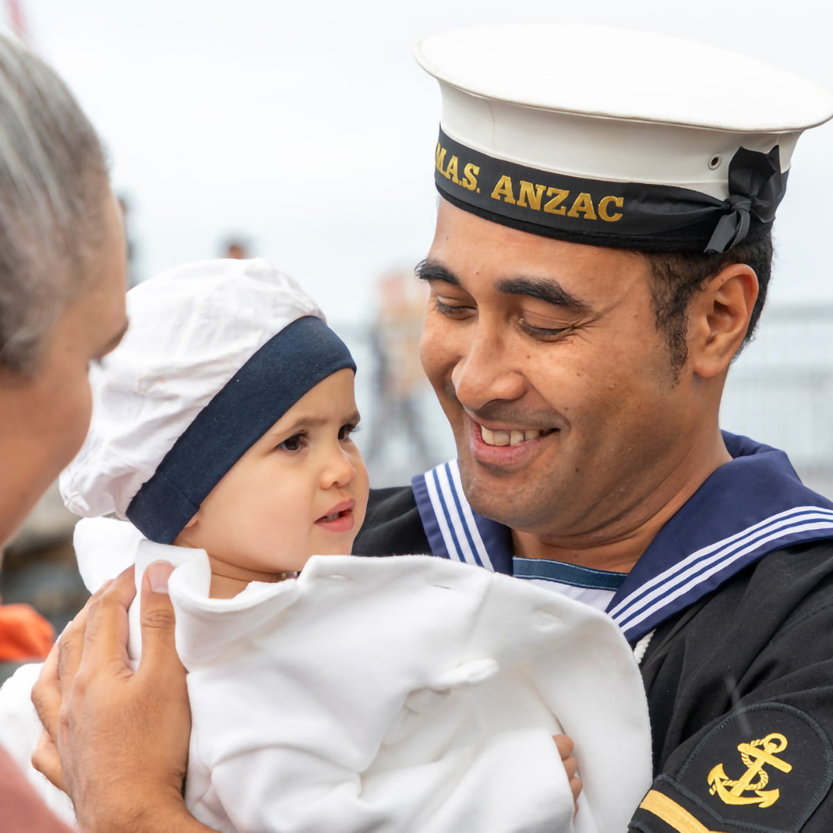 A man in the navy looking happily at his small child.