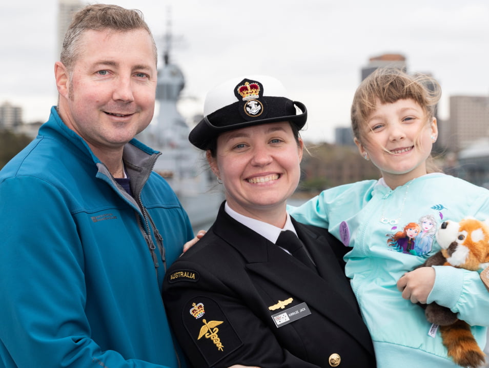 Women in formal military uniform stands with daughter and husband.
