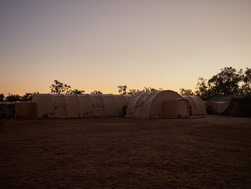 The sun rises over a row of tents in the outback.