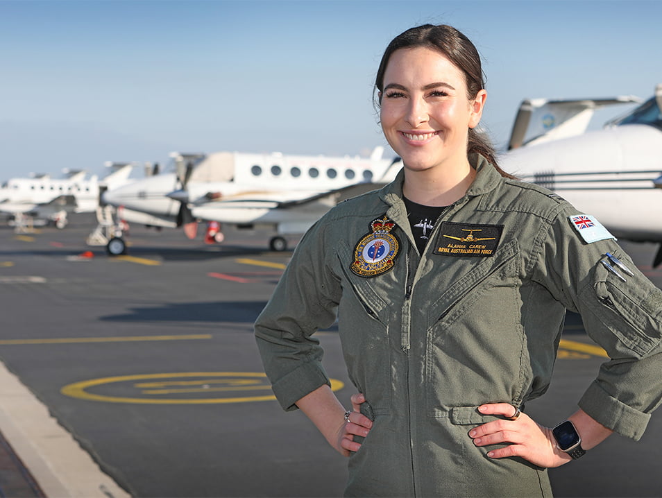 A women in the Air Force  stands on the runway in front of aircraft.