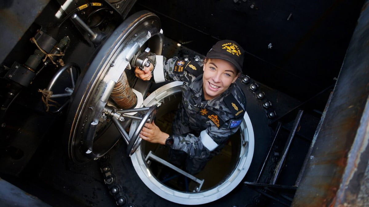 A Navy member climbing out of a submarine smiling. 