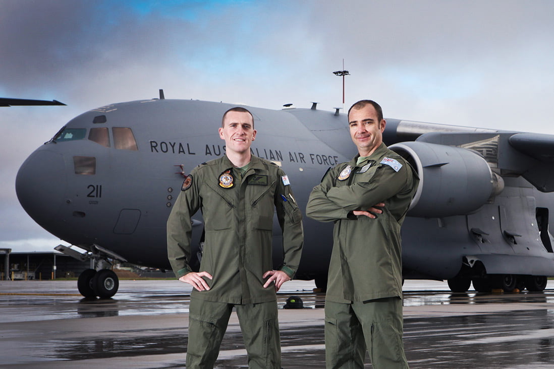 Two members of the Air Force stand proudly on the runway in front of a huge plane.